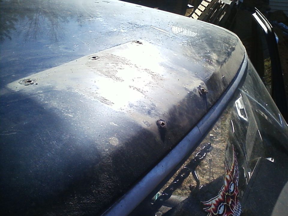 Close-up of a vehicle's hood and windshield, showing some rust spots and a chain