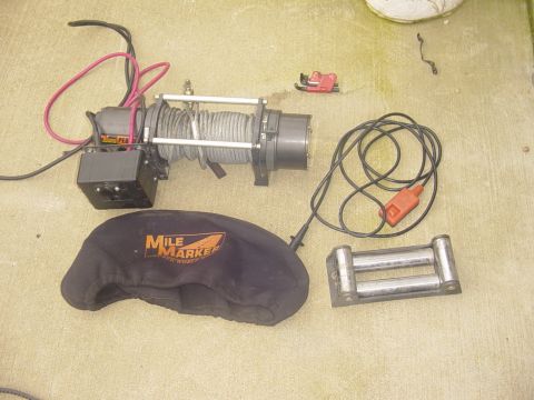 1989 Ford Bronco - A winch, its protective cover, and a roller fairlead are laid out on a concrete surface.