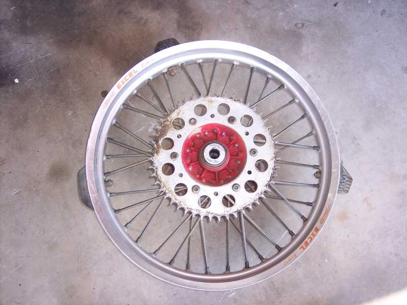 Motorcycle rear wheel with silver Excel rim, spokes, white hub plate and red center hub on concrete
