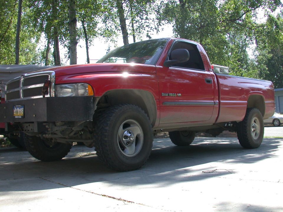 Red Dodge Ram 1500 pickup, 3q-front view, lifted with steel bumper and off-road tires.