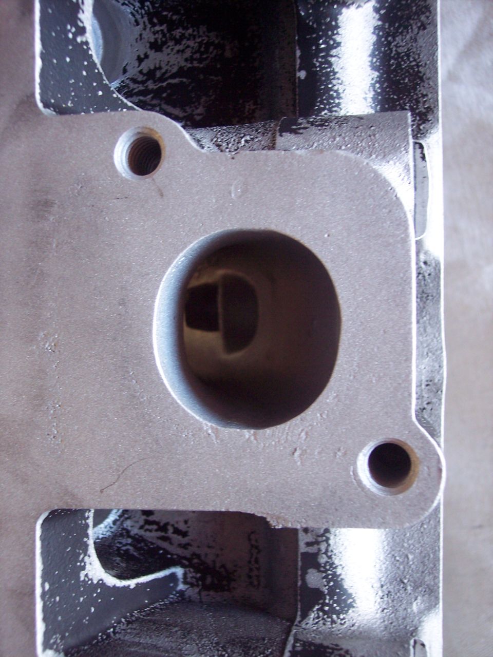 Close-up of an engine cylinder head intake or exhaust port. The metal surface shows some casting marks and a threaded bolt hole nearby