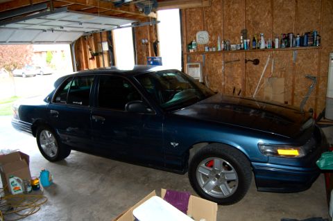 1985 Mercury Grand Marquis - Dark blue sedan with a fender badge is parked inside a garage.