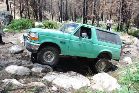 1996 Ford Bronco - This green Ford Bronco is shown off-roading over large rocks in a wooded area.