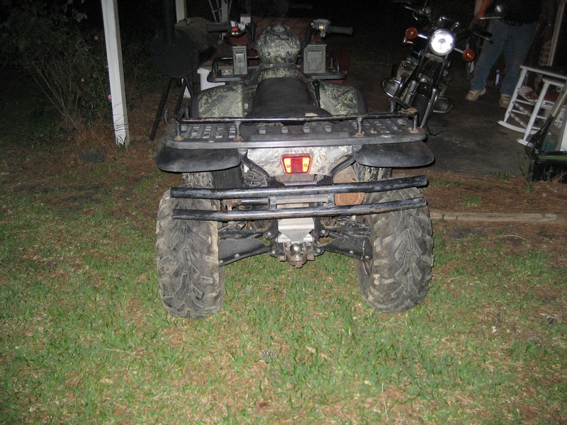 Rear view of a camouflage ATV with a tow hitch and a motorcycle in the background