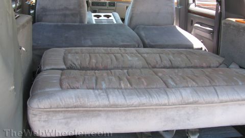 1996 Ford C-350 (Centurion Conversions) - Interior of a conversion-truck cabin shot through the open rear door, with the gray velour rear bench folded flat into a bed alongside a se…