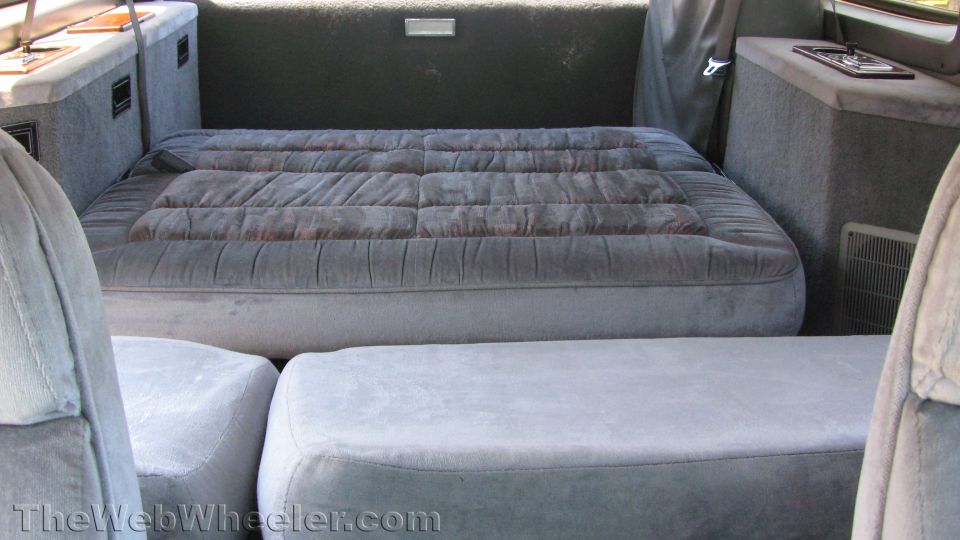 Gray cloth rear seats folded flat into a bed inside a conversion SUV