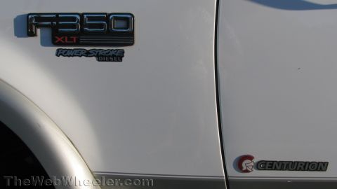 1996 Ford C-350 (Centurion Conversions) - Close-up of the white front fender and door on a Ford truck showing the chrome "F-350 XLT" badge with a "Power Stroke Diesel" emblem below…