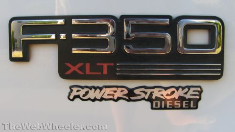 1996 Ford C-350 (Centurion Conversions) - Close-up of the chrome-on-black F-350 XLT fender badge on a white Ford truck, with a Power Stroke Diesel emblem mounted directly below it.…