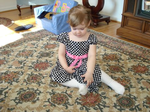 2000 Ford Crown Victoria - A young child in a black and white polka dot dress with a pink sash sits on a large, ornate rug in a living room.