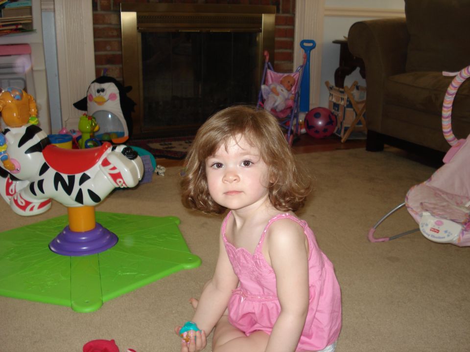 Child in pink dress sits on carpet with toys, including a zebra ride-on