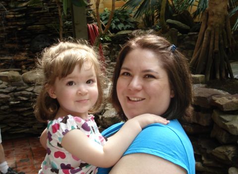 2000 Ford Crown Victoria - A woman holds a young child in front of a stone wall and tropical plants.