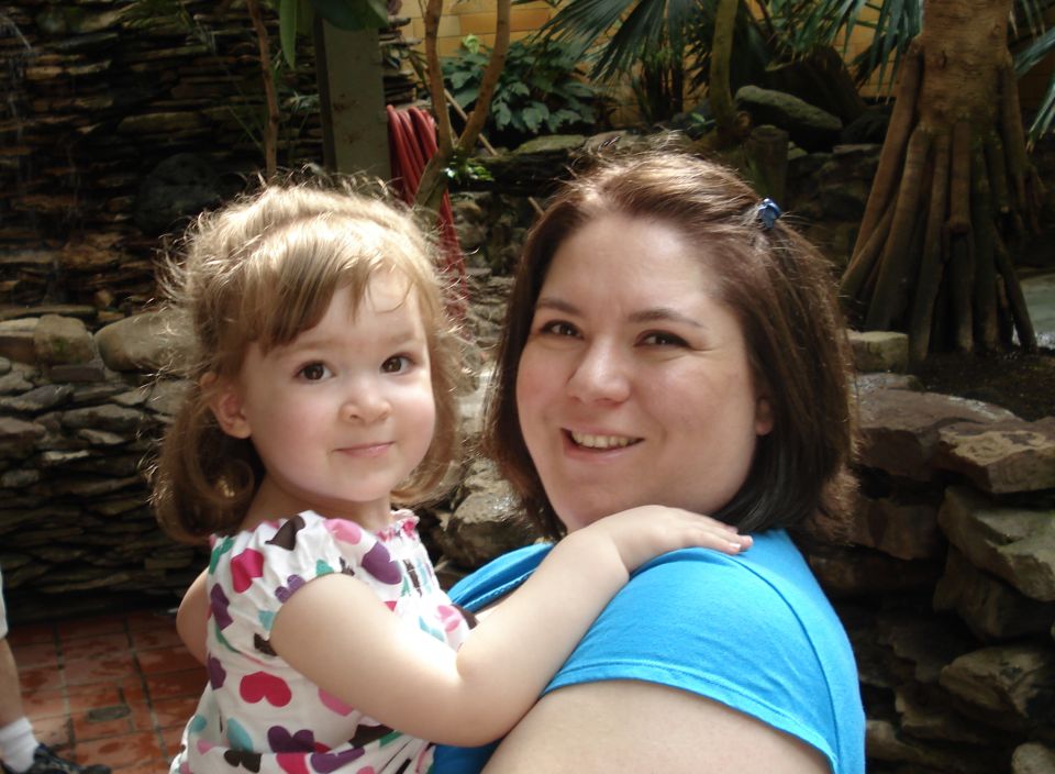 Woman in a blue shirt holds a young girl with pigtails wearing a white shirt with colorful hearts