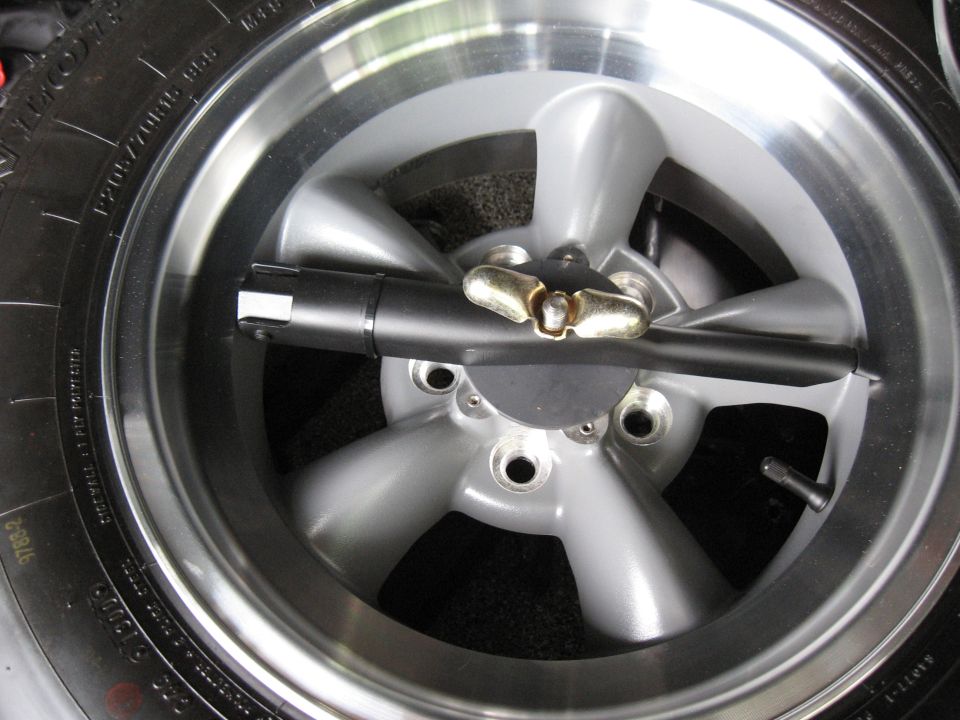 Close-up of a silver five-spoke wheel with a tire and lug nut tool