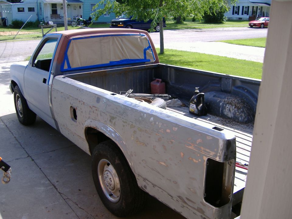 Pickup truck body is stripped and taped off for painting. Tools and fluids are in the bed
