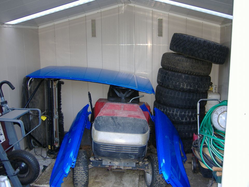 Blue truck hood and fenders stored in a shed with stacked off-road tires