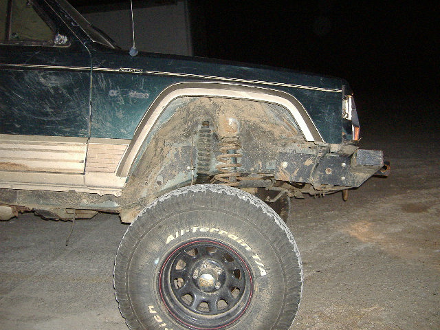 Green 1993 Jeep Cherokee front fender and tire covered in mud, with visible suspension components
