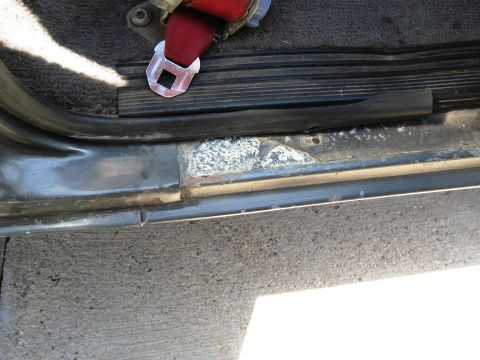 1986 Ford Bronco - Close-up of a vehicle's interior door sill showing wear and a seatbelt buckle.