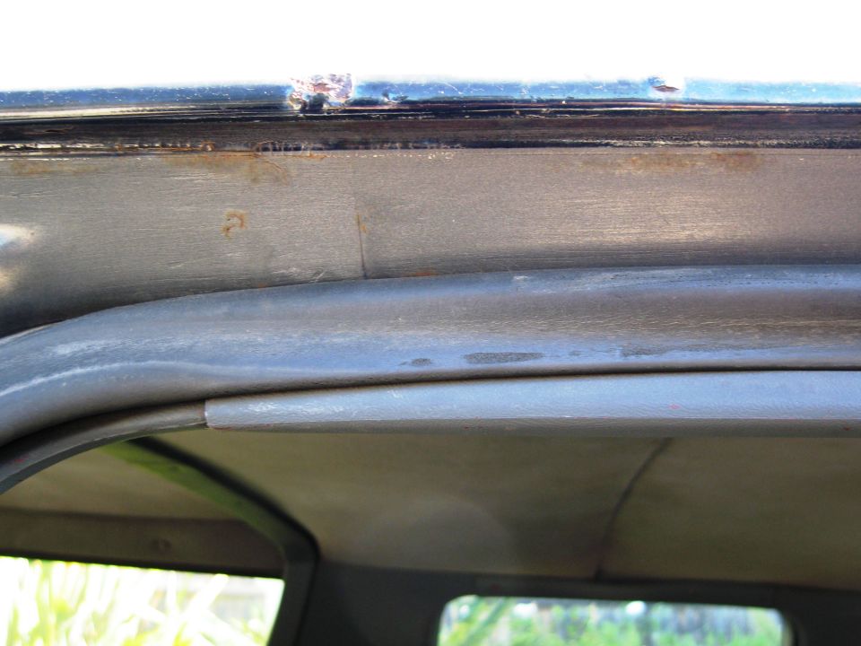 Close-up of the interior roofline of a vehicle, showing some rust and wear on the metal trim above the door frame