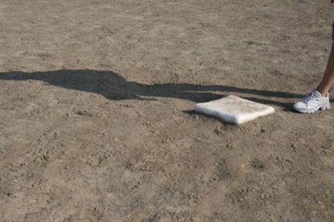 1990 Chevrolet Suburban - A shadow stretches across a baseball field near home plate, with a person's legs and sneakers visible.
