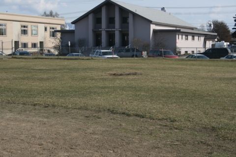 1990 Chevrolet Suburban - Multiple vehicles are parked in front of a building with a large grassy area in the foreground.