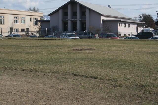 Several cars and a van parked on a grassy area in front of a building