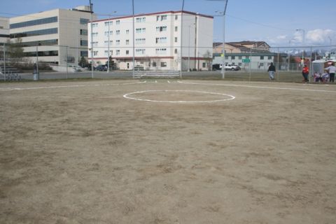 1990 Chevrolet Suburban - A view of a softball field with buildings and people in the distance under a clear sky.