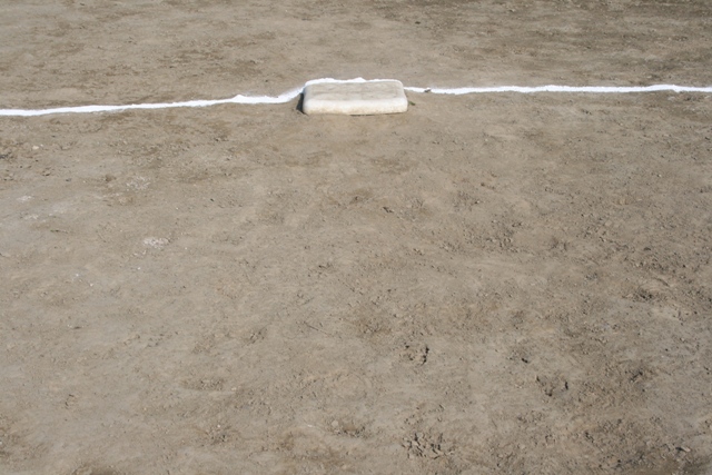baseball base on dirt infield with white foul line