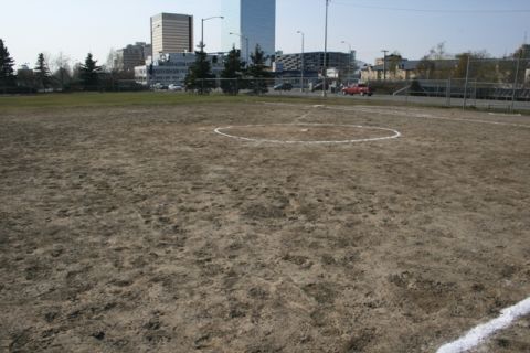 1990 Chevrolet Suburban - A baseball field is shown with city buildings in the distance under a clear sky.