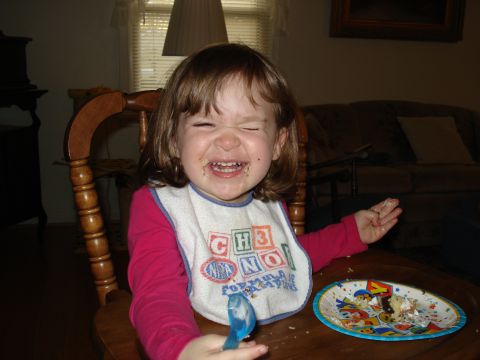 2000 Ford Crown Victoria - A young child with a very happy, messy face enjoys a plate of cake, complete with a blue spoon and a colorful bib.
