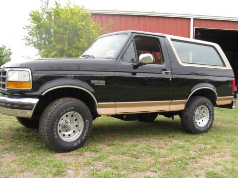 1994 Ford Bronco - This black Ford Bronco features tan trim and is parked on a grassy area with a red barn in the background.