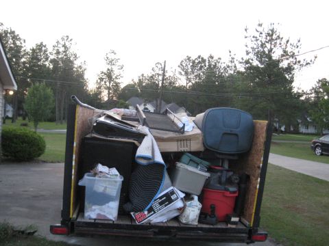1900 Ford C-350 (Centurion Conversions) - A trailer is filled with various discarded items, including electronics, storage bins, and a red shop vac.