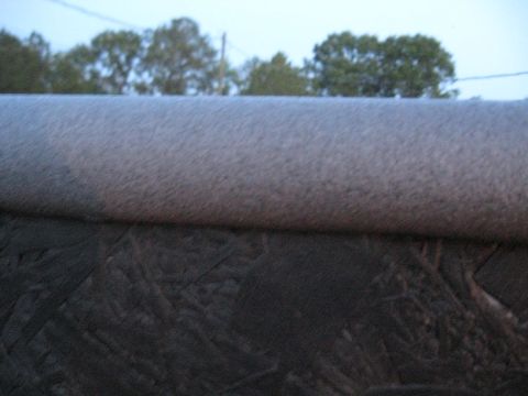1900 Ford C-350 (Centurion Conversions) - A close-up view shows a textured gray surface above a dark, rough material, with trees visible in the background.