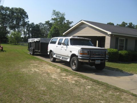 1900 Ford C-350 (Centurion Conversions) - A white Ford Bronco SUV is parked in a driveway, hitched to a covered utility trailer.