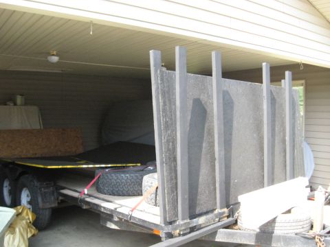1900 Ford C-350 (Centurion Conversions) - A trailer is parked inside a garage, loaded with construction materials and a spare tire.