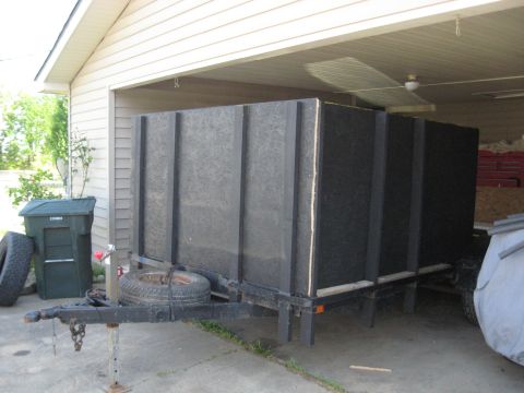 1900 Ford C-350 (Centurion Conversions) - An enclosed trailer is parked in front of a garage, with a trash can and spare tire nearby.