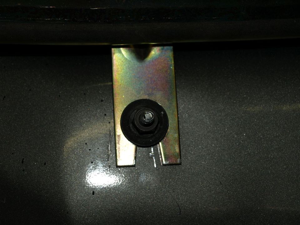 Close-up of a metal bracket and bolt on a dark gray surface. Supermotors.net logo visible