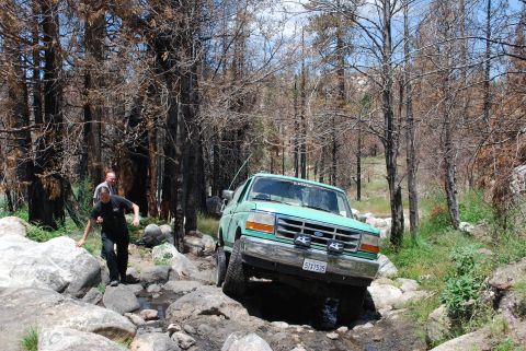 1996 Ford Bronco - 1996 Ford Bronco off-roading through a rocky stream in a wooded area.