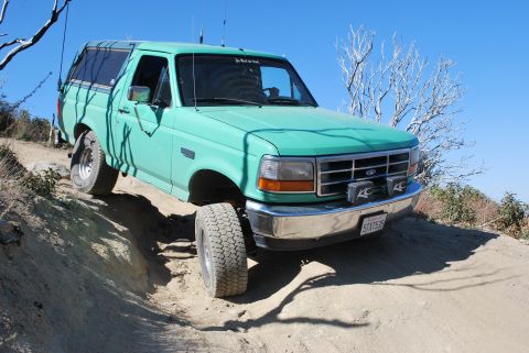 1996 Ford Bronco - A green 1996 Ford Bronco navigates a steep dirt path under a clear blue sky.