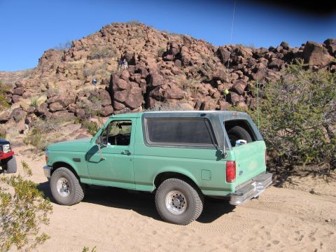 1996 Ford Bronco - A green Ford Bronco is parked on a dirt road with a rocky hill behind it.