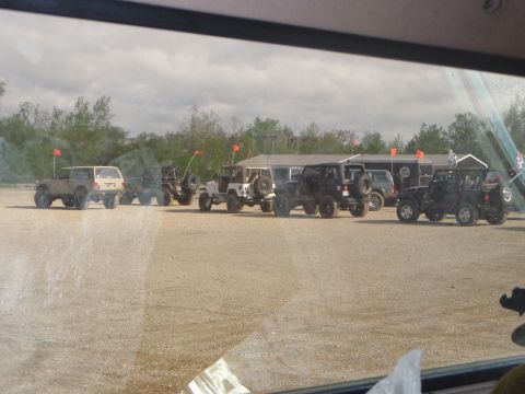 1996 Ford Bronco - A collection of off-road vehicles are gathered in an outdoor lot under a cloudy sky.
