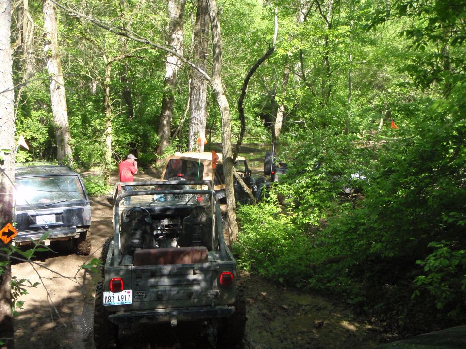 Rear view of a camouflage Jeep Wrangler on a muddy trail, with other vehicles behind