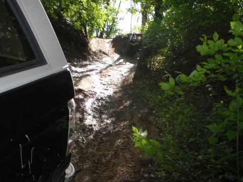 1996 Ford Bronco - Two vehicles navigate a muddy off-road trail through a wooded area.
