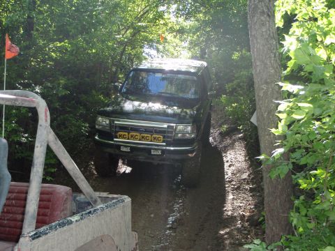 1996 Ford Bronco - A 1996 Ford Bronco navigates a dirt path surrounded by dense foliage, with another off-road vehicle in view.
