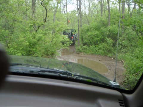 1996 Ford Bronco - Another vehicle navigates a muddy path through a wooded area, viewed from the perspective of a driver inside a different vehicle.