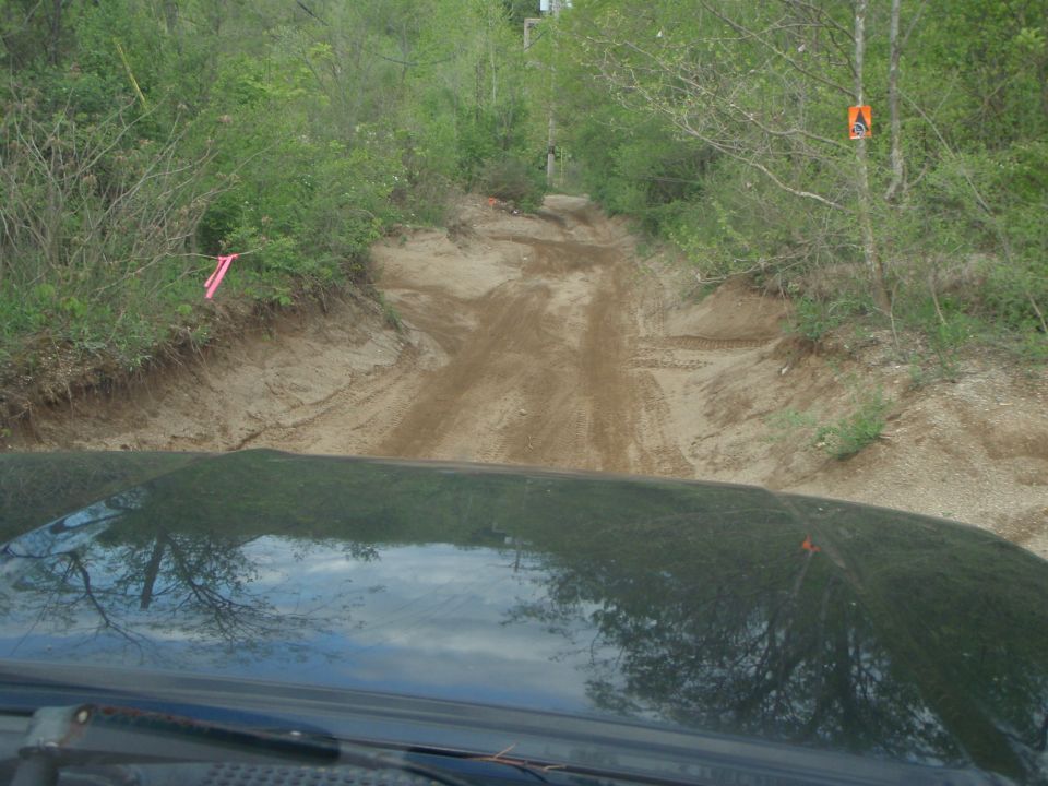 View from inside a vehicle looking at a sandy, rutted off-road track through trees