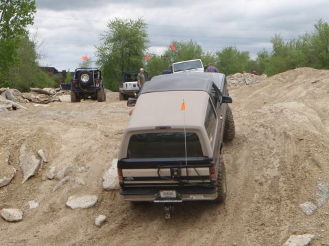 1996 Ford Bronco - Several off-road vehicles navigate a challenging dirt course with rocky terrain.