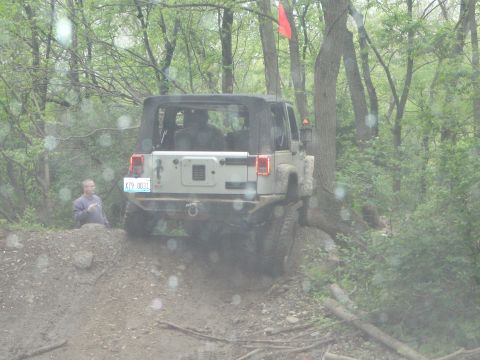 1996 Ford Bronco - A Jeep Wrangler navigates a muddy, wooded trail with a person standing nearby.