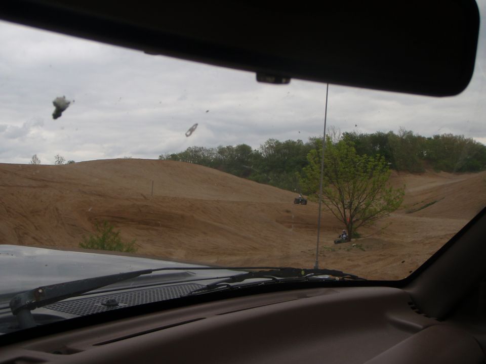View from inside a vehicle looking out at a sandy off-road park with ATVs on the trails