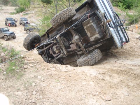 1996 Ford Bronco - An SUV has rolled onto its side on a rough terrain course, with several other off-road vehicles visible in the background.