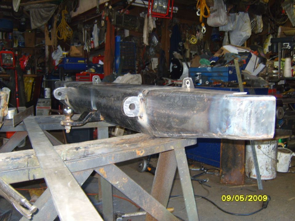 Black metal rear bumper with tow hitch, mounted on sawhorses in a workshop